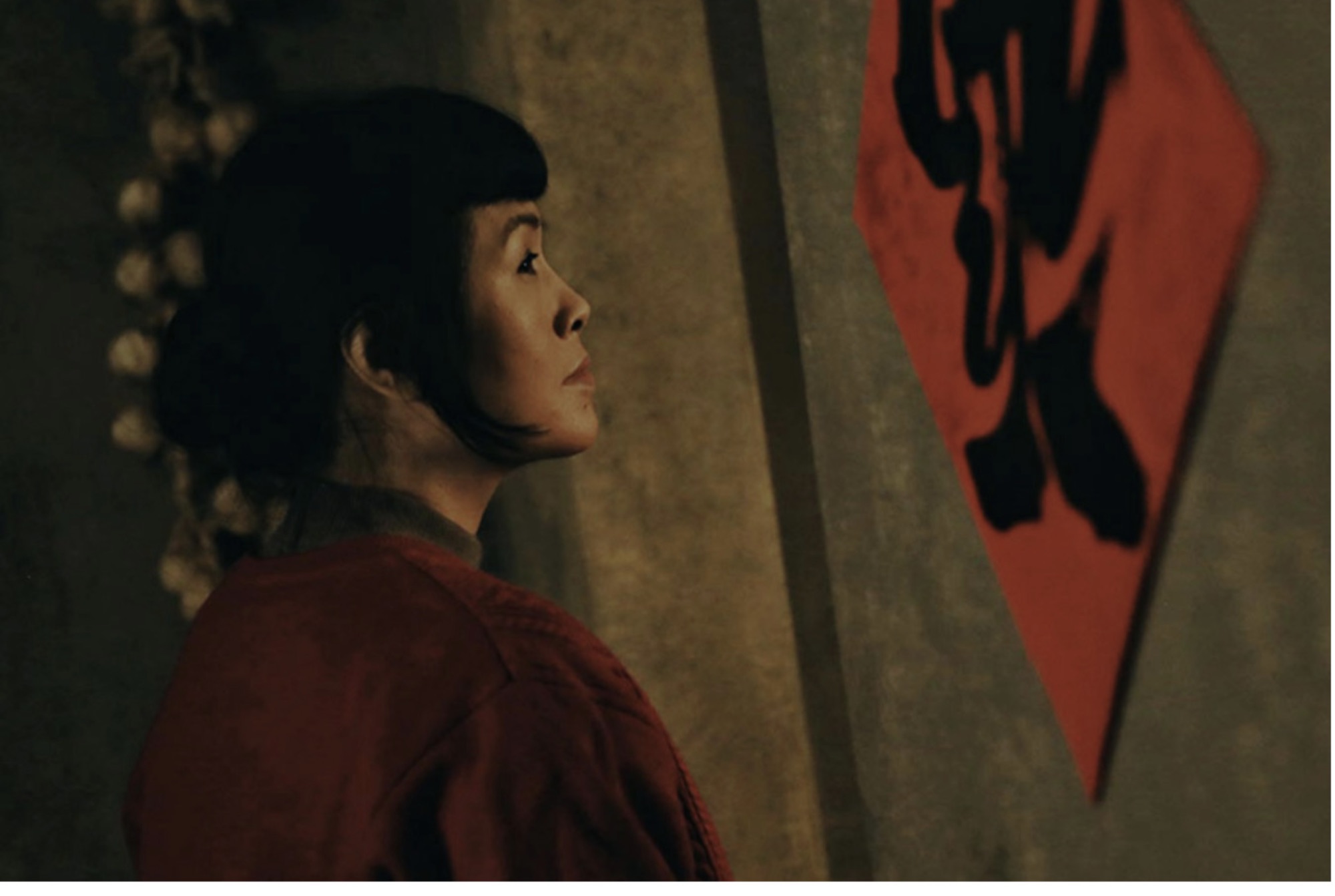 Film still of Grace Chang in a deep red costume beside a calligraphy banner